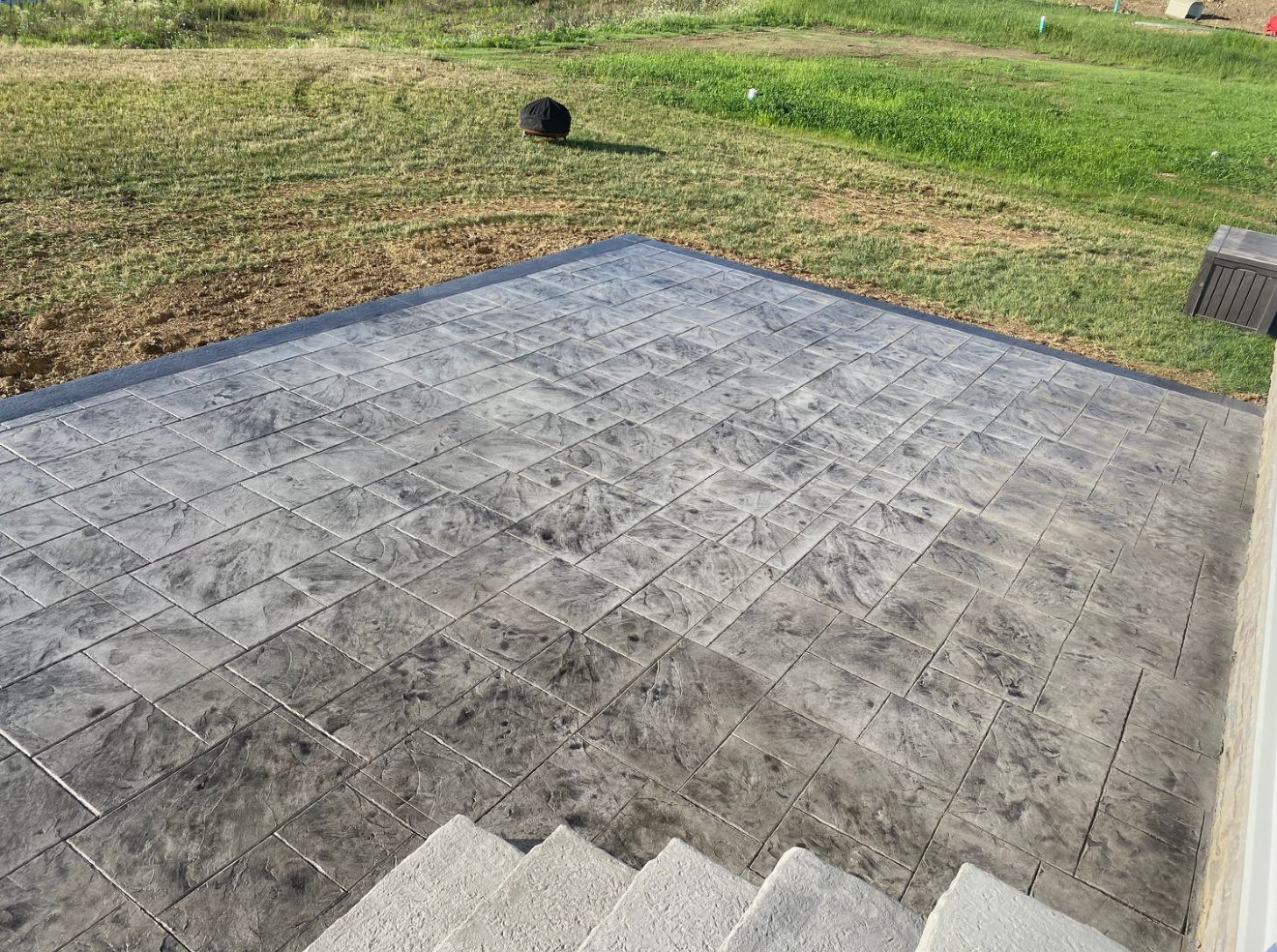 Gray patterned concrete patio with steps and lawn.