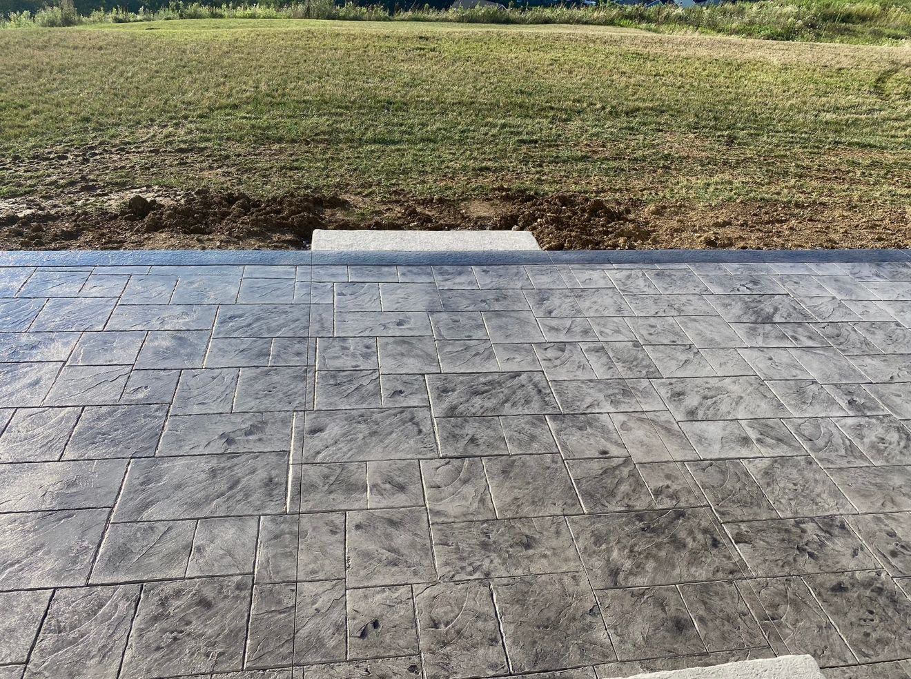 Gray stamped concrete patio leading to a grassy yard.