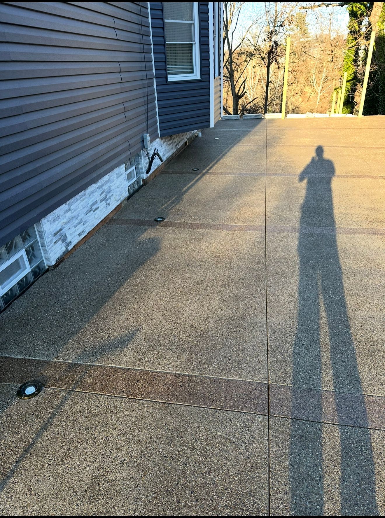 Concrete driveway next to a blue house, with a person's shadow cast on it.