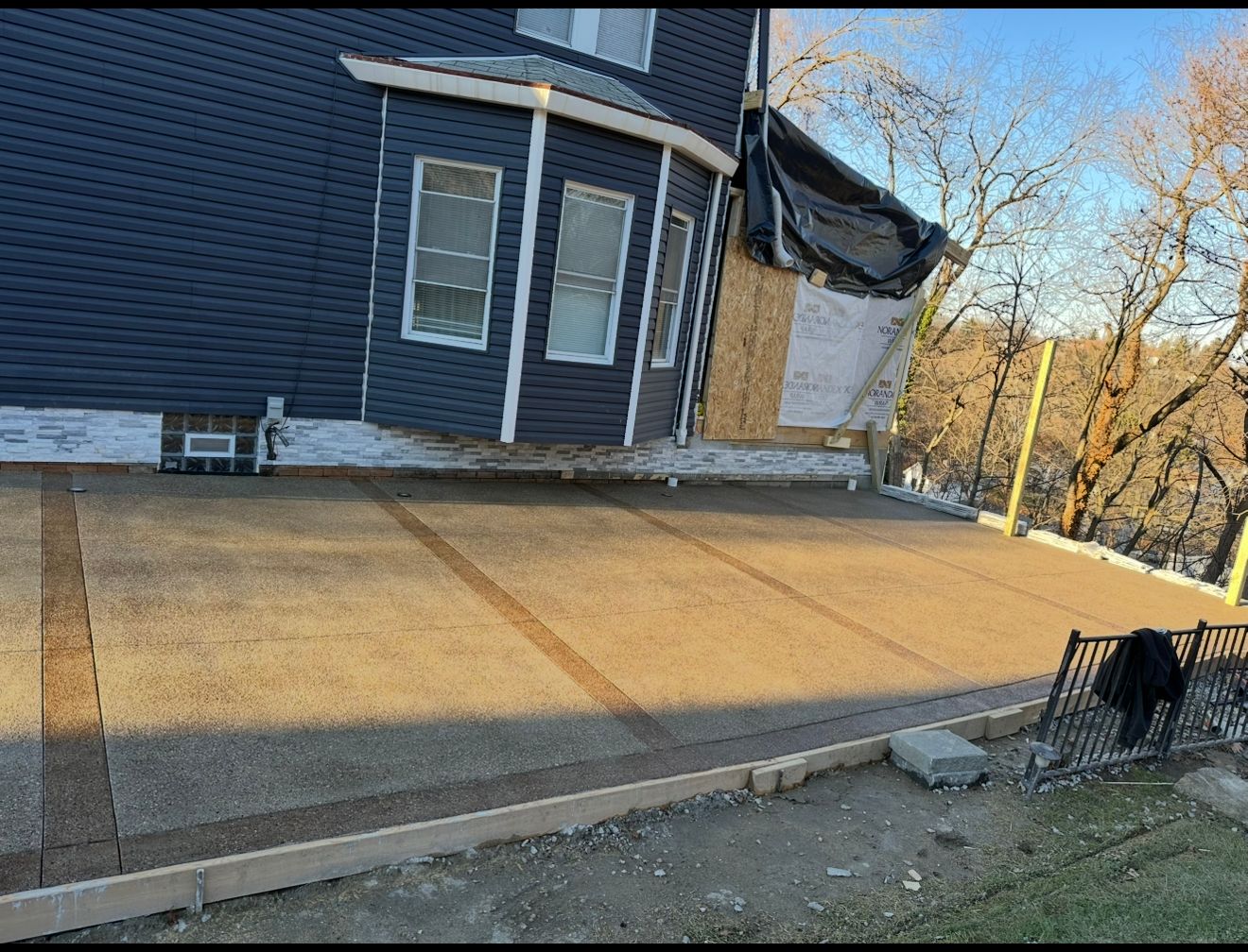 Exterior view of a house with a newly poured concrete driveway featuring tan and brown accents.
