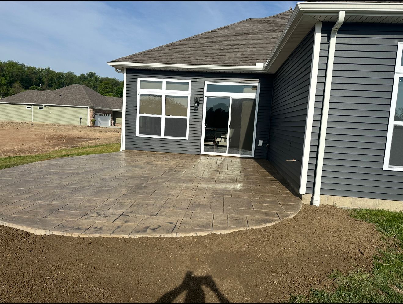 Back patio with stamped concrete, adjacent to a gray house with a sliding glass door and windows.