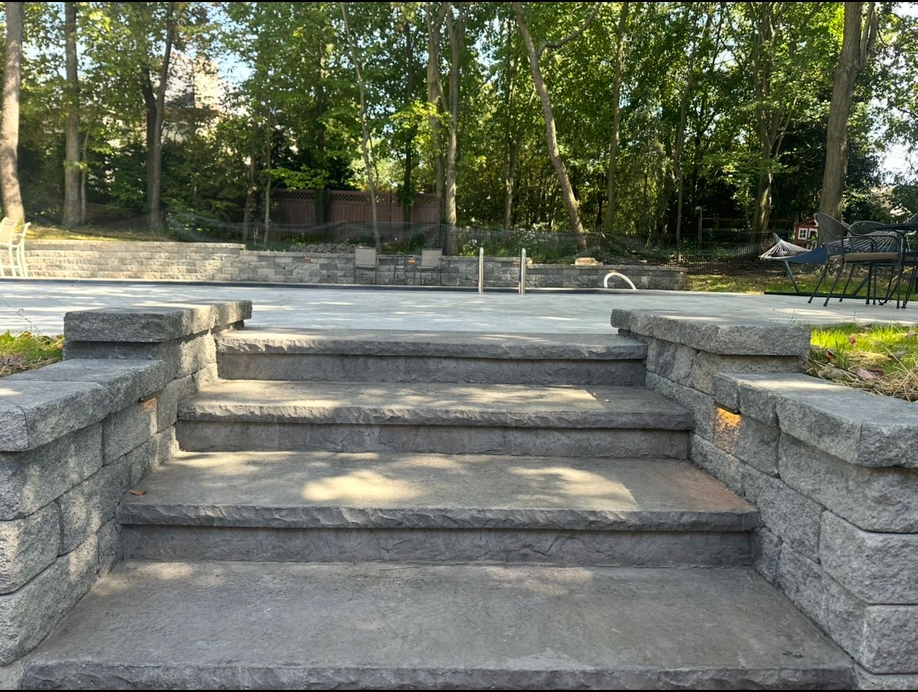 Stone steps lead to a patio area, surrounded by brick walls and greenery.
