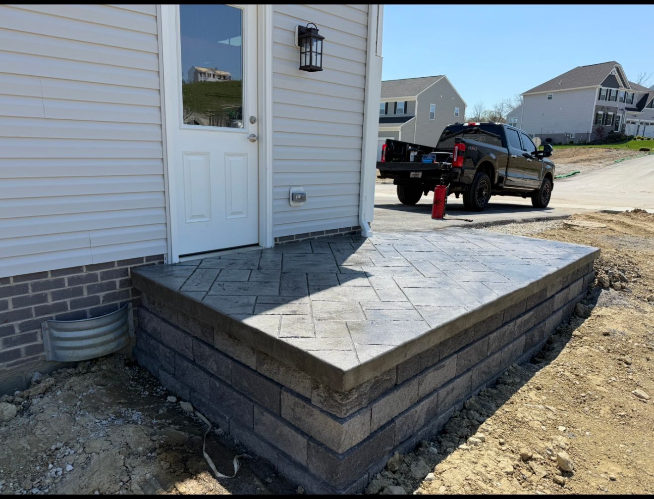 Concrete porch with brick facade next to a house with a truck parked on a dirt lot.