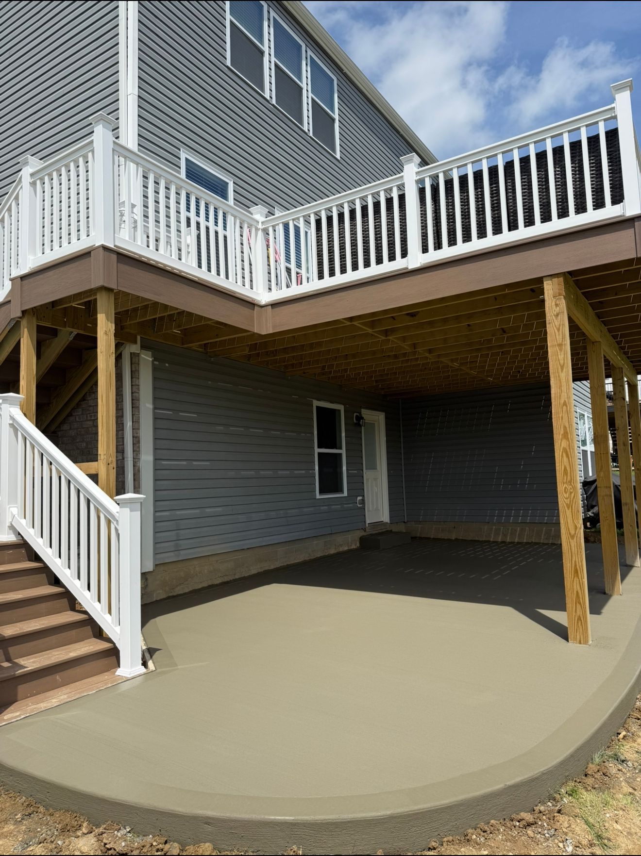 Gray house with a two-level deck. The lower level is a concrete patio under the upper deck.