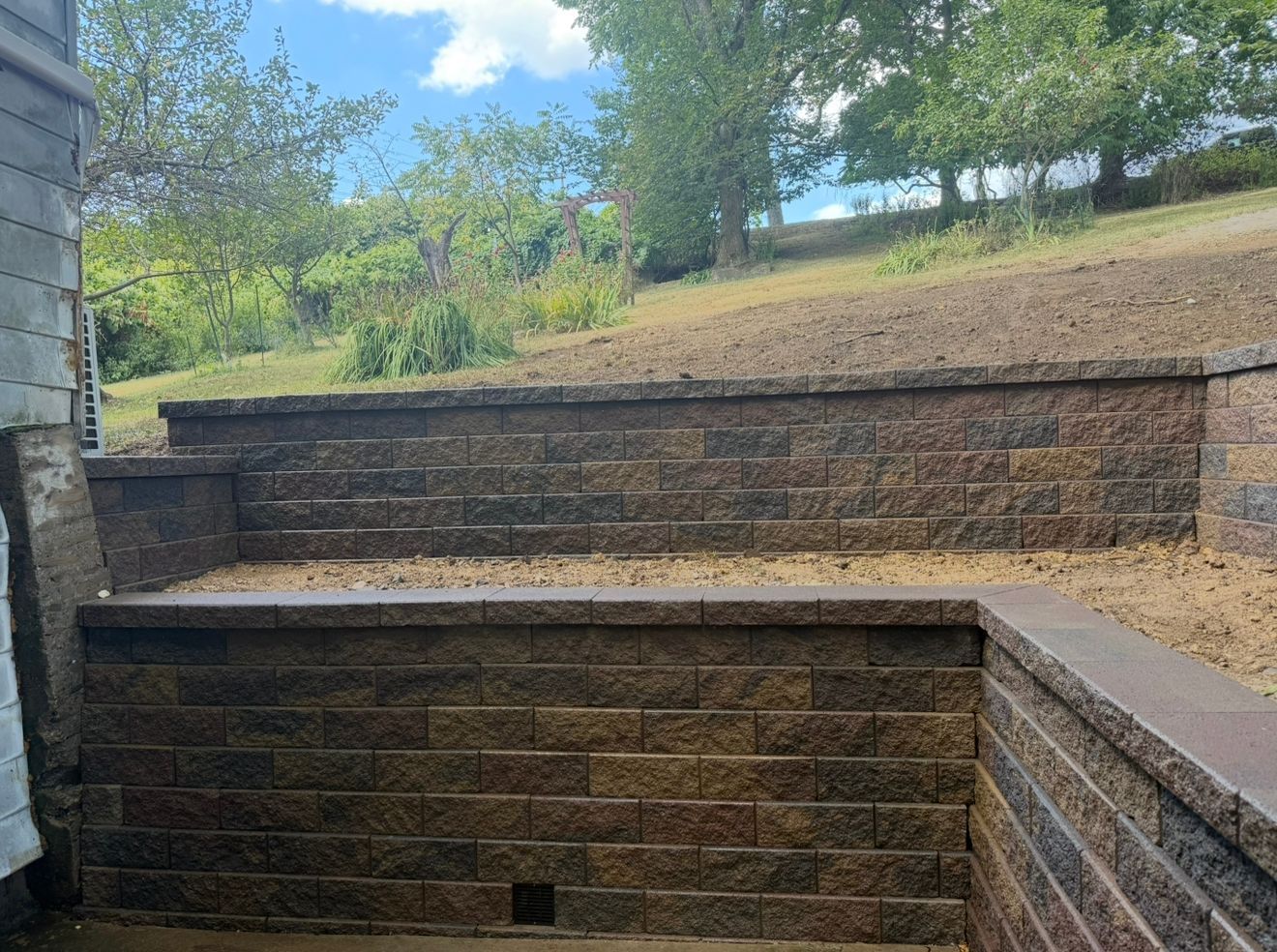 Stone retaining wall with steps leading up a hillside, sunny outdoor setting.