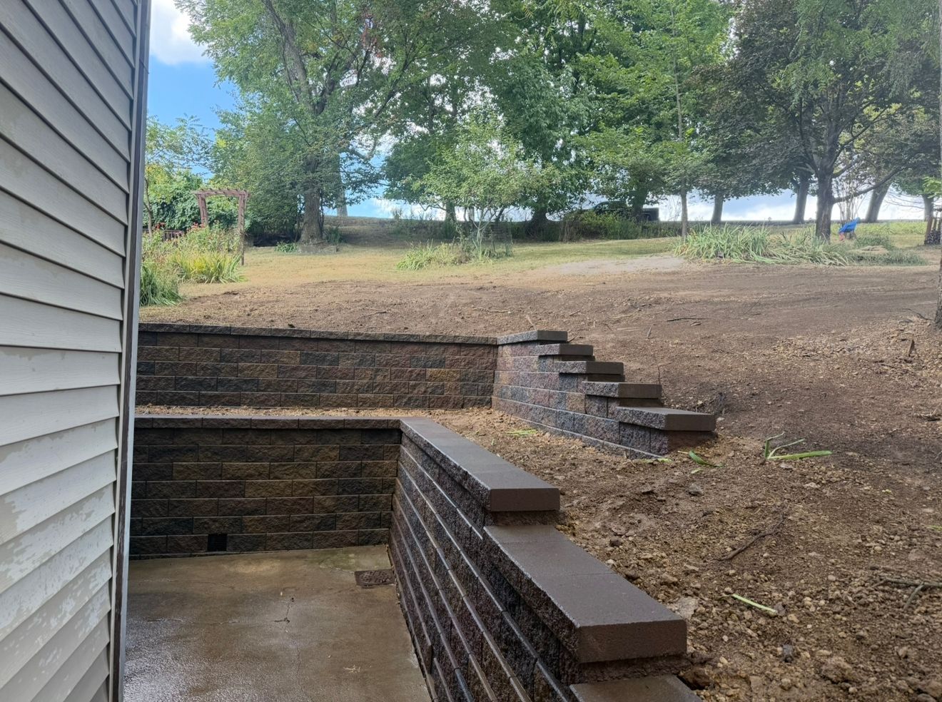 Outdoor view with retaining wall and steps leading to grassy area under trees.
