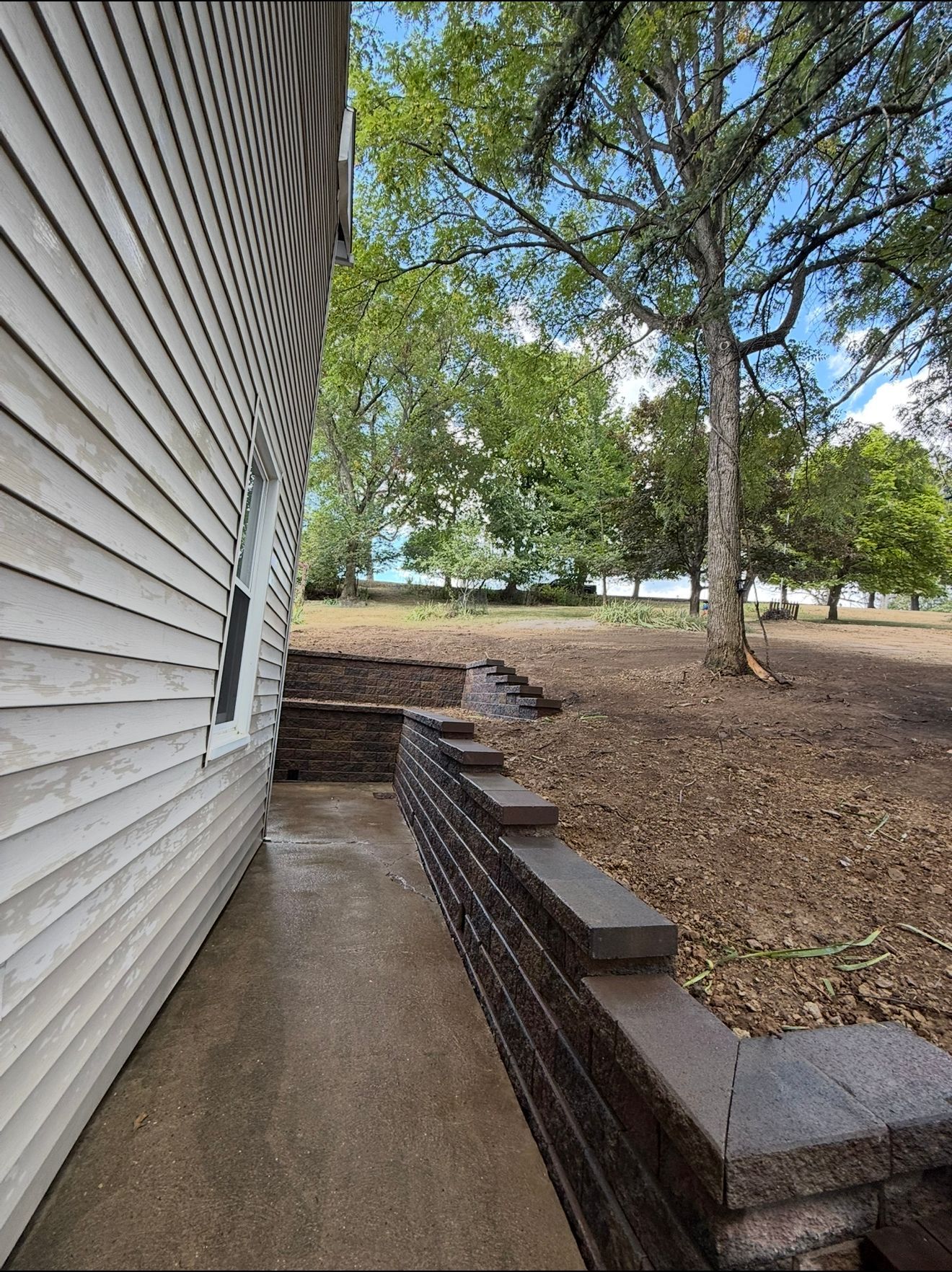 Exterior of a house with a retaining wall, steps, and a view of trees and a field.