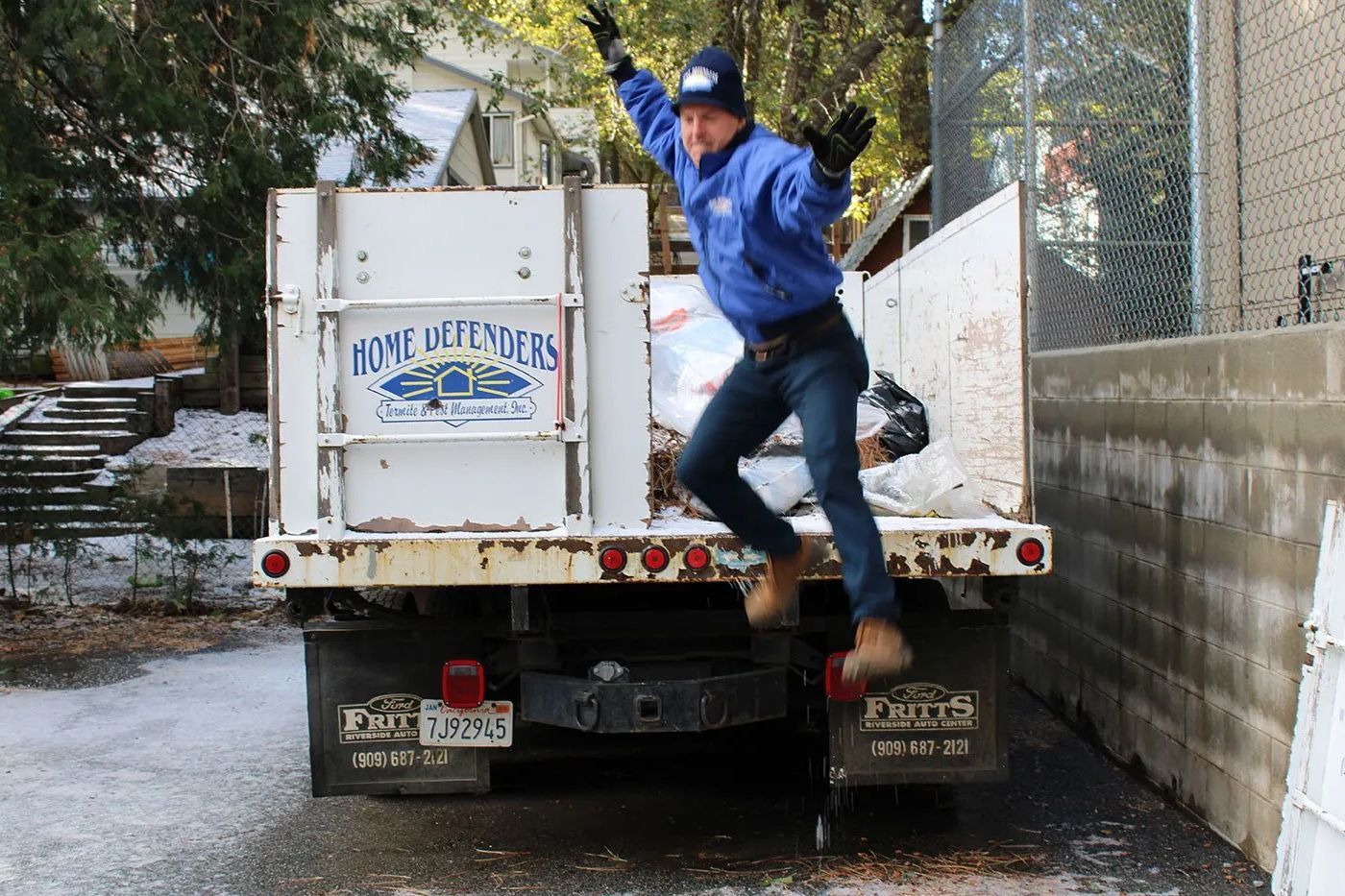 Man in blue jacket jumping from the back of a white truck in a snowy driveway