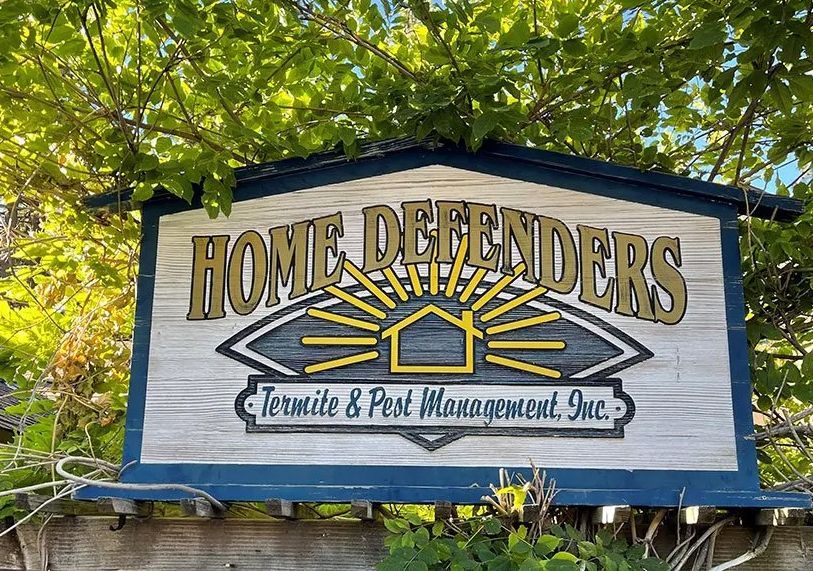 Home Defenders sign with house logo and “Track & Pest Management, Inc.” on a blue-and-white banner outdoors