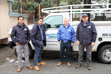 Four workers in dark jackets stand beside a white service van on a wet street.