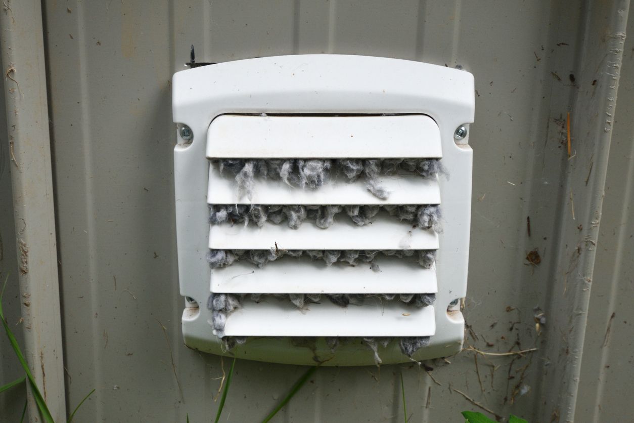 White wall vent with horizontal slats covered in dark mold or debris on a weathered exterior wall