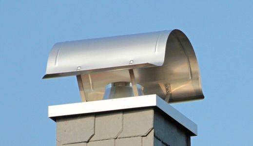 Silver rooftop ventilation vent on a brick chimney against blue sky
