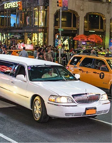 White limousine on a city street, yellow taxis, people walking, evening scene.
