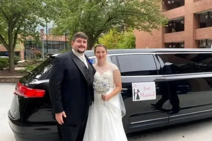 Newlyweds pose beside a black limousine with a 