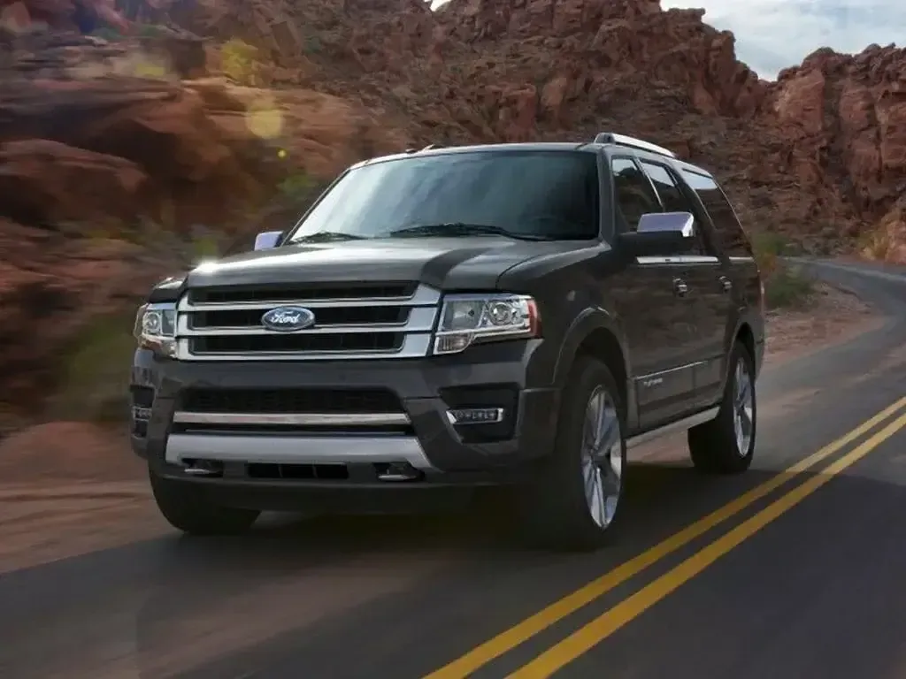 Dark gray Ford Expedition SUV on a winding road in a desert landscape.