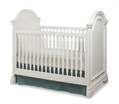 White crib with decorative arched headboard and footboard, blue skirt.