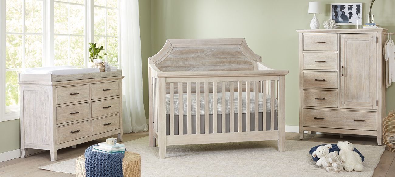 Nursery furniture set with a crib, changing table, and dresser in a light wood finish.