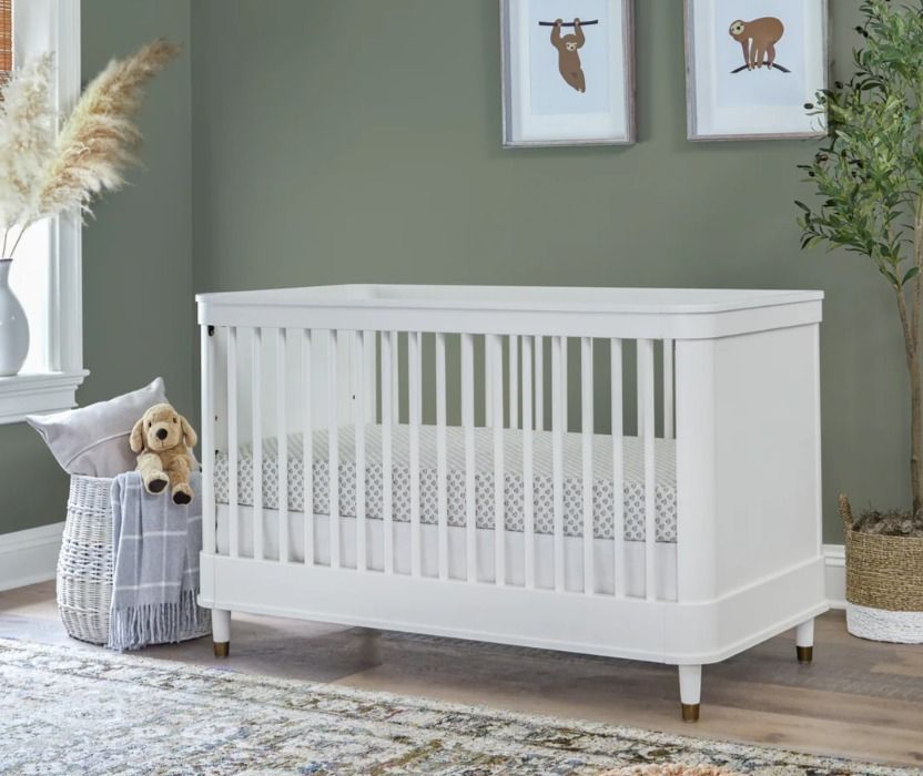White crib in a nursery with wall art and a potted plant.