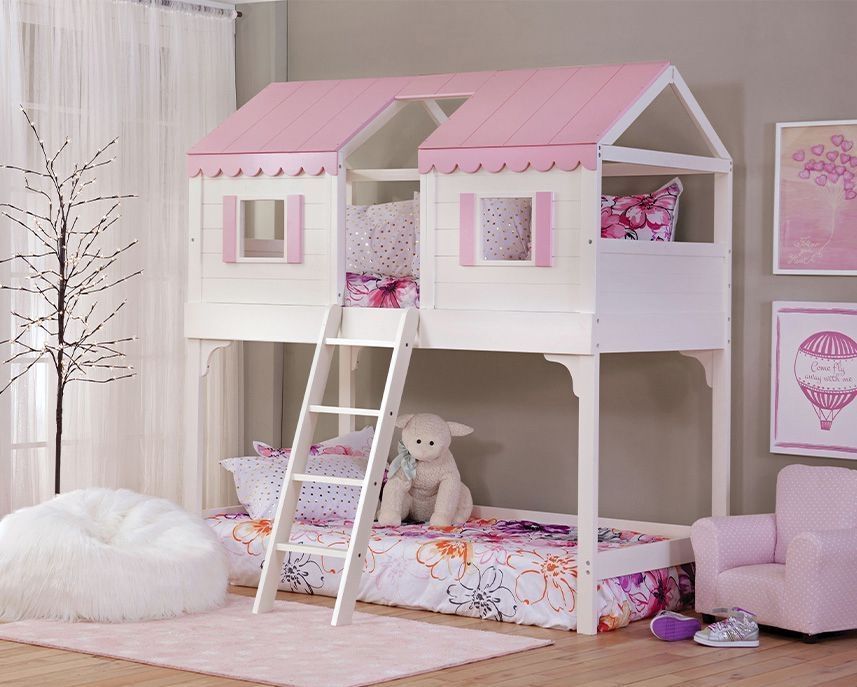 Pink and white house-shaped bunk bed with a ladder, set in a light-colored bedroom, with pink accents and decor.