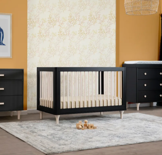 Black crib and furniture set in a nursery with light wood accents and a patterned rug.