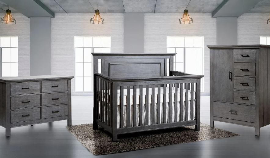 Gray nursery furniture set including a crib, dresser, and wardrobe on a rug.