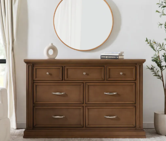 Wooden dresser with seven drawers, round mirror, and decorative items.