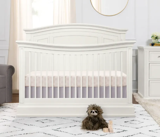 White crib with a curved headboard, a plush toy, and a rug.