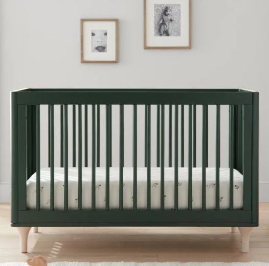 Green crib with wooden slats and a mattress in a nursery, with framed art on the wall.