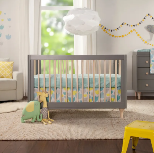 Gray crib in a nursery with pastel decor and a white cloud light fixture.