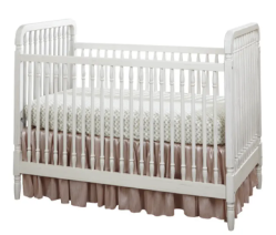 White wooden baby crib with a pink skirt, mattress, and bedding.
