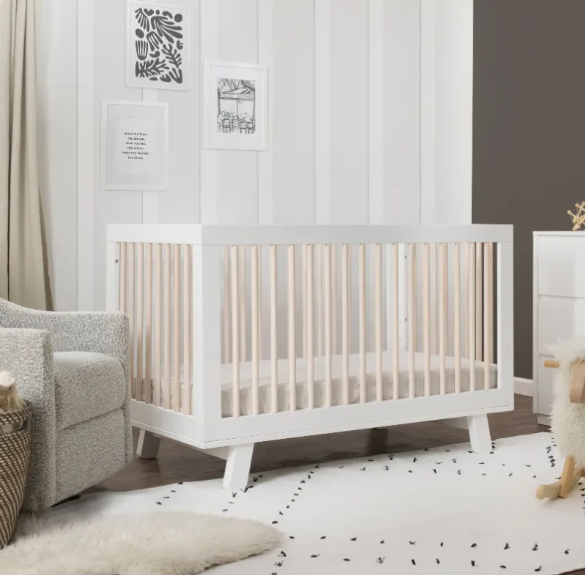 White crib in a nursery, with a rocking chair and rug.