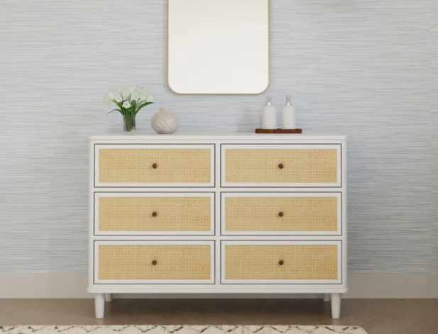 White dresser with six drawers, cane webbing, and gold knobs. A mirror and decor sit above.