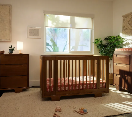 A nursery with a wooden crib, dressers, and a window with natural light.