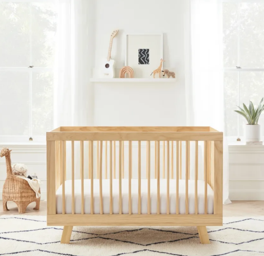 Wooden crib in a nursery, with decor on a shelf and a woven giraffe toy.