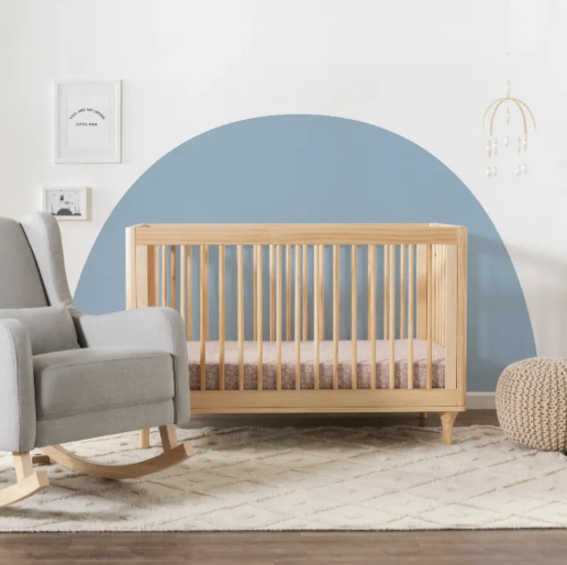 Nursery with a crib, rocking chair, and ottoman on a patterned rug; blue semi-circle on the wall.