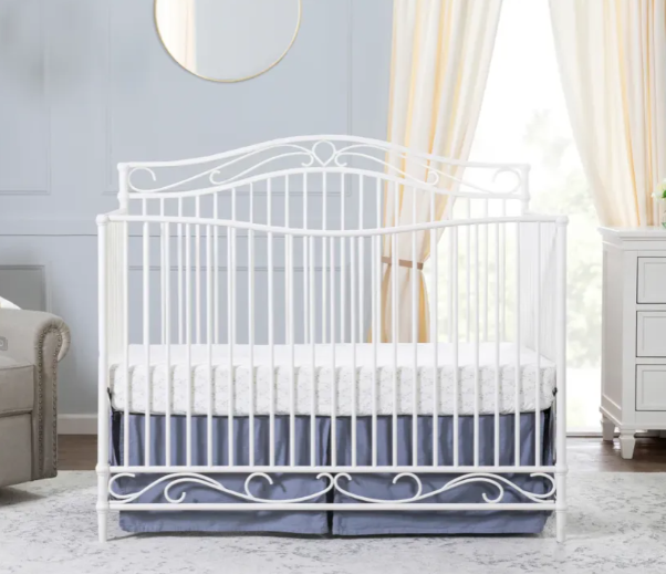 White metal crib with blue crib skirt in a light-filled nursery.