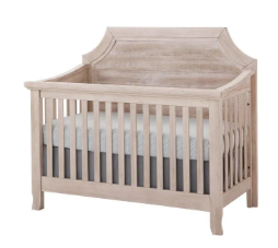 Light-colored wooden crib with a scalloped headboard, holding a mattress and gray crib skirt.