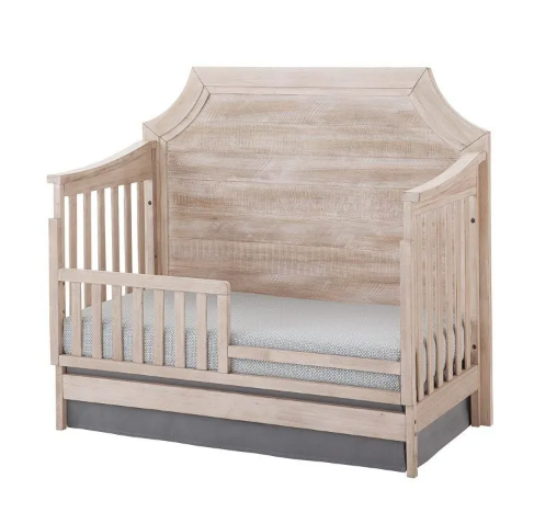 Wooden toddler bed with a headboard, light finish, and a gray bed skirt.
