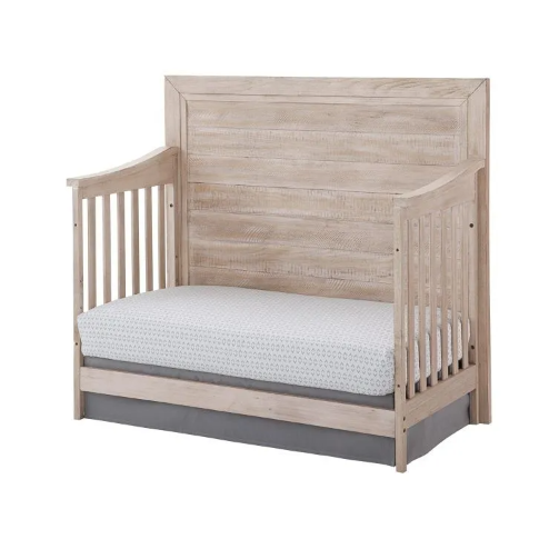 Wooden crib with a mattress and gray crib skirt.