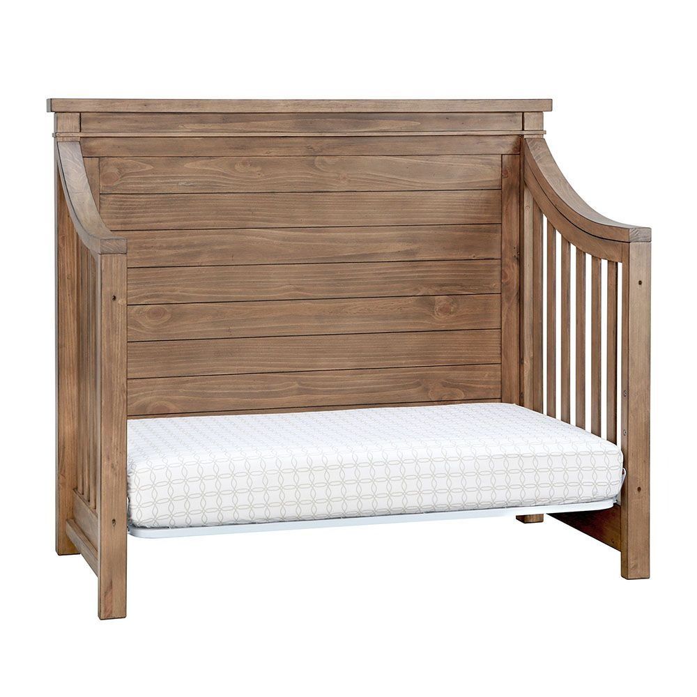 Wooden daybed with slatted back and curved sides, containing a mattress.