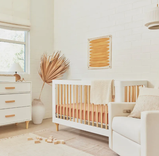 White nursery with crib, dresser, and glider; peach accents.