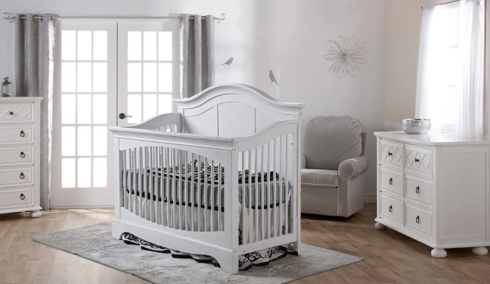 White nursery furniture set: crib, dresser, chair, in a bright room.