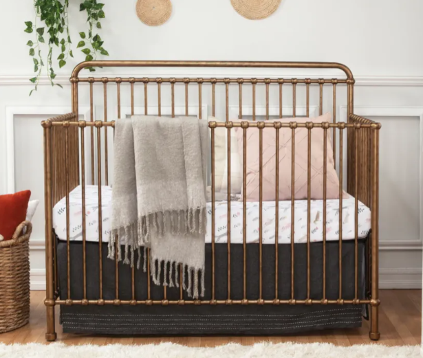 Gold metal crib with bedding, blanket, and pillows.