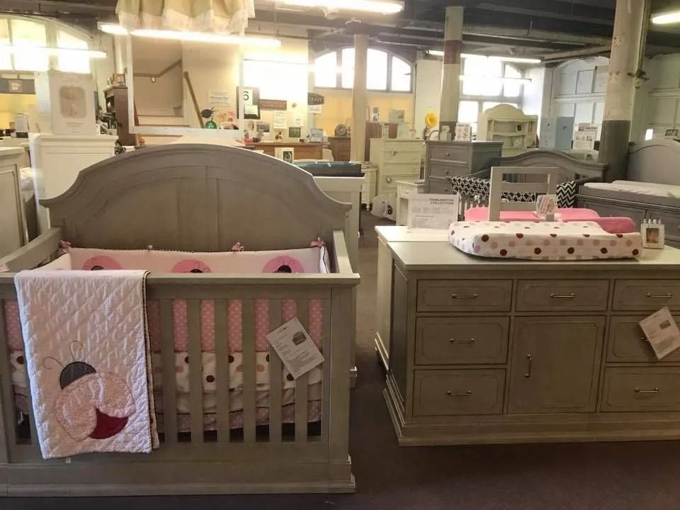 Grey nursery furniture display with crib and dresser, soft pink bedding.