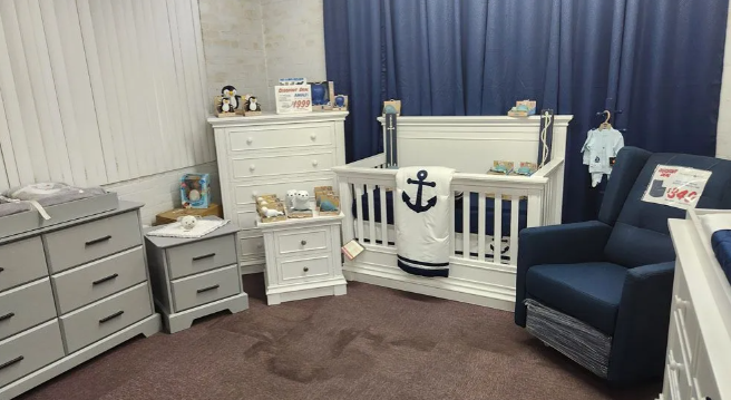 Nautical-themed nursery: white crib, dresser, glider with navy accents, brown carpet, blue curtains.