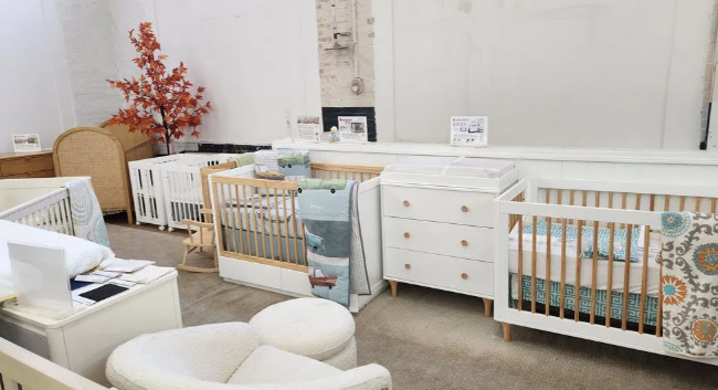 Nursery furniture showroom: cribs, changing table, and chair displayed in a bright, modern space.