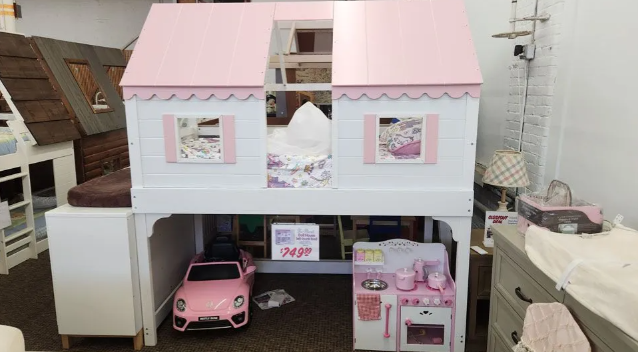 Pink and white playhouse bed with car and toy kitchen underneath, displayed in a store.