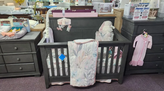 Baby crib with bedding, mobile, and stuffed animals displayed in a furniture store.