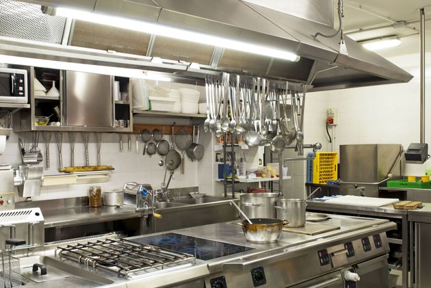 Commercial kitchen with stainless steel stove, hanging utensils, and cooking pots under bright lights
