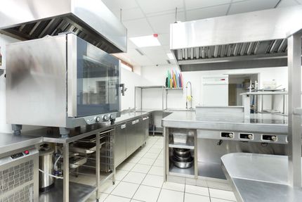 Bright commercial kitchen with stainless steel counters, ovens, sinks, and tiled floor